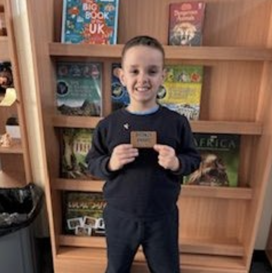 A student smiling, holding up a bronze badge